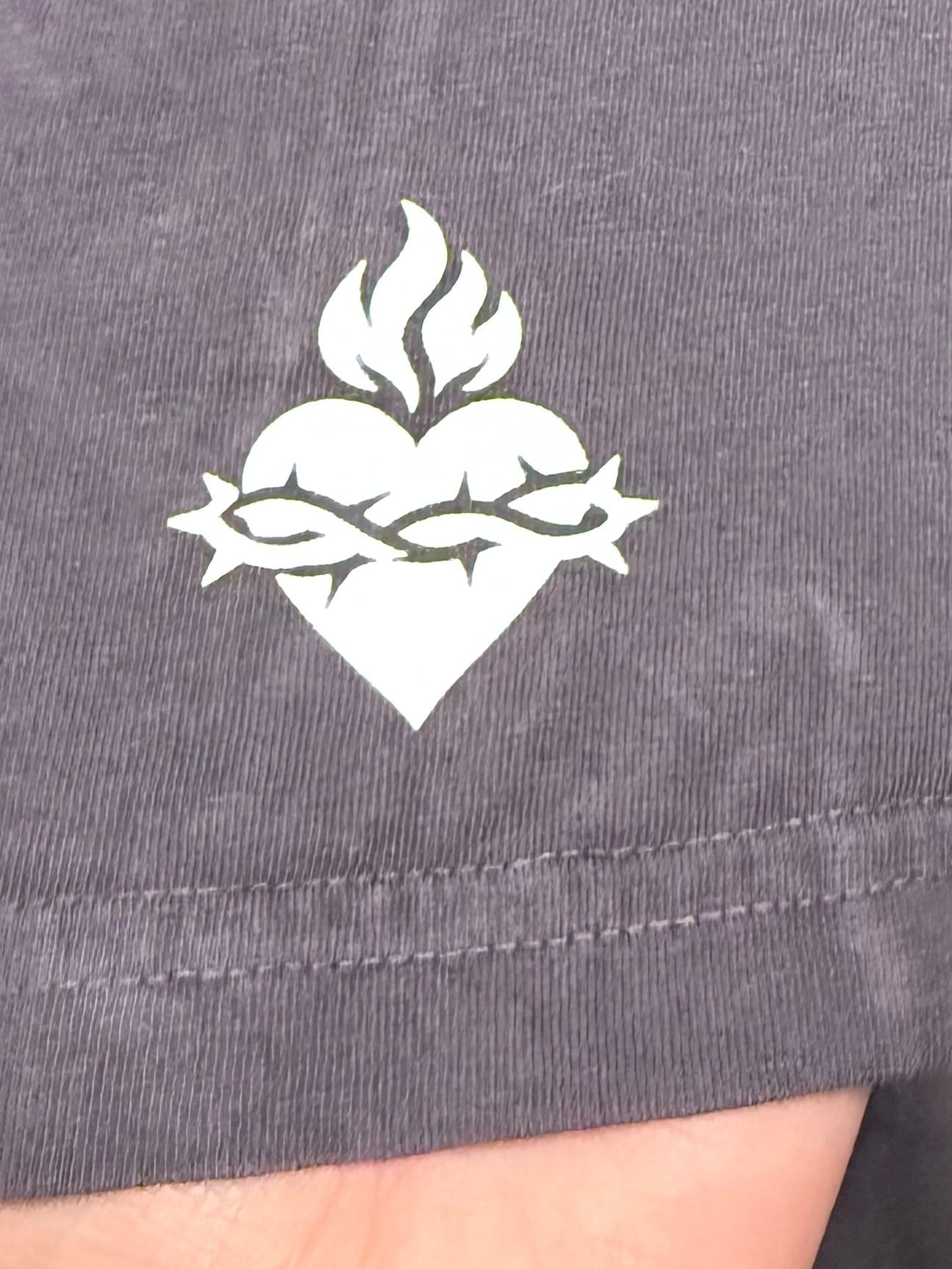 The side of a graphite t-shirt that shows a sacred heart logo in white on the sleeve