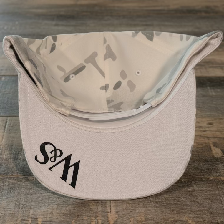 The underneath of a white camo snapback that has the logo W&S in black on the bill
