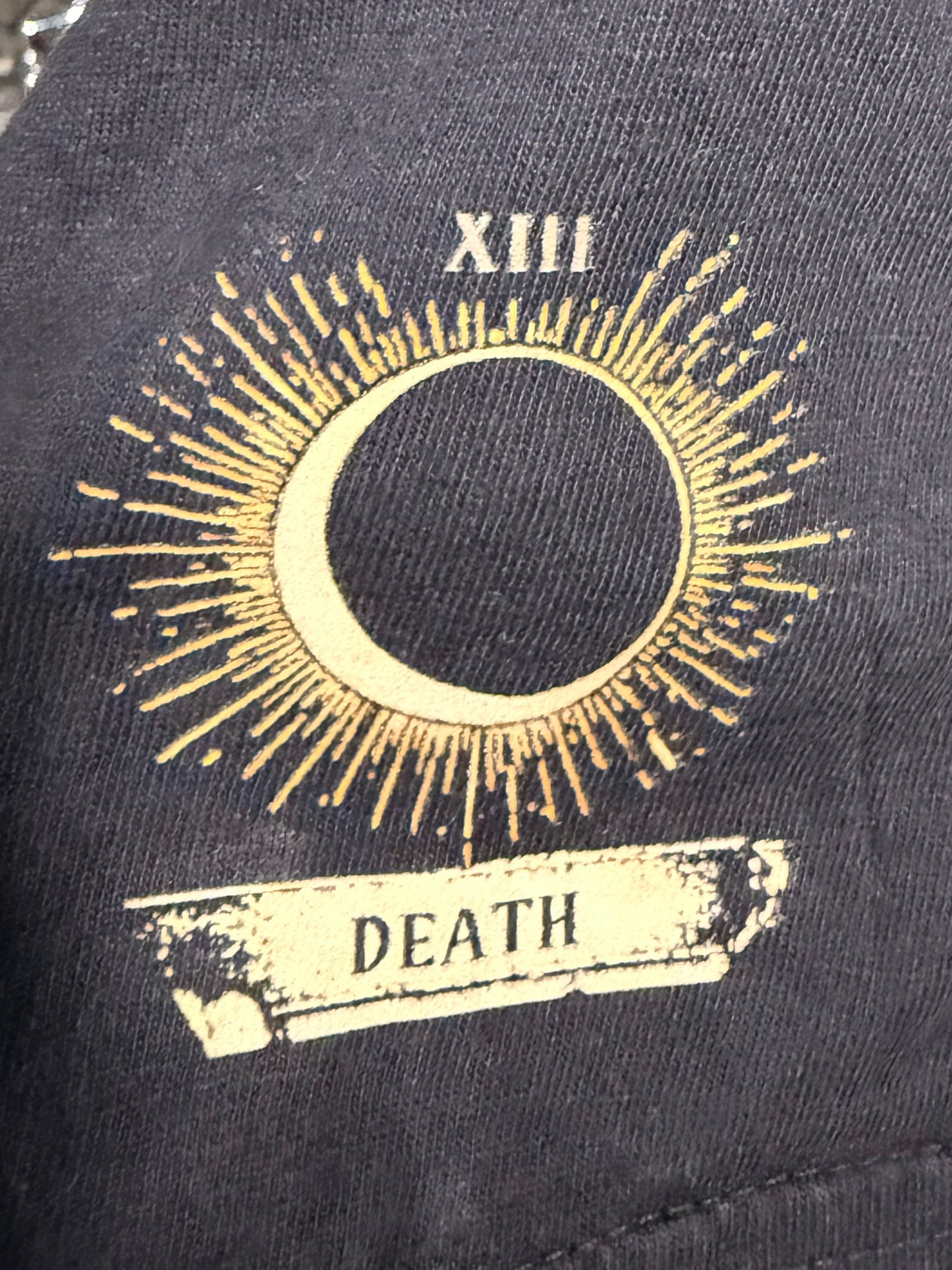 Black t-shirt arm sleeve with a logo in gold that shows a new moon with the text XIII and "Death 
