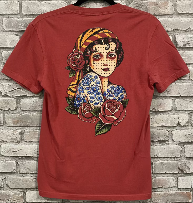 A chili shirt that has an image of a traditional tattoo inspired Gypsy Girl, against a grey brick background