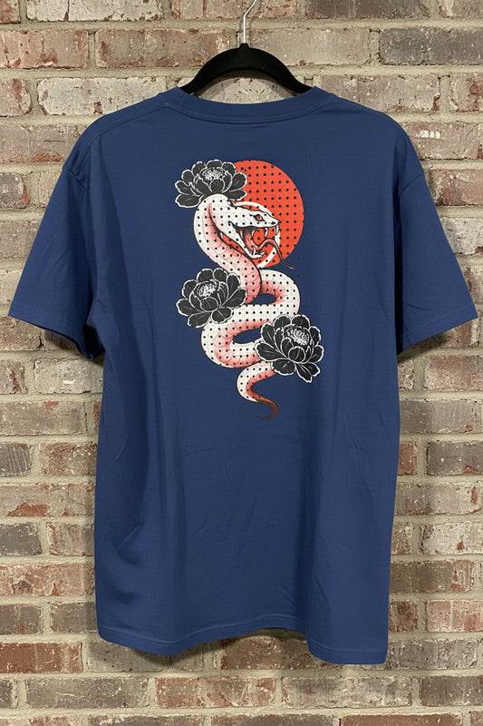The back of a true navy t-shirt that has a design on a white and pink snake with black peonies and red moon against a grey brick background