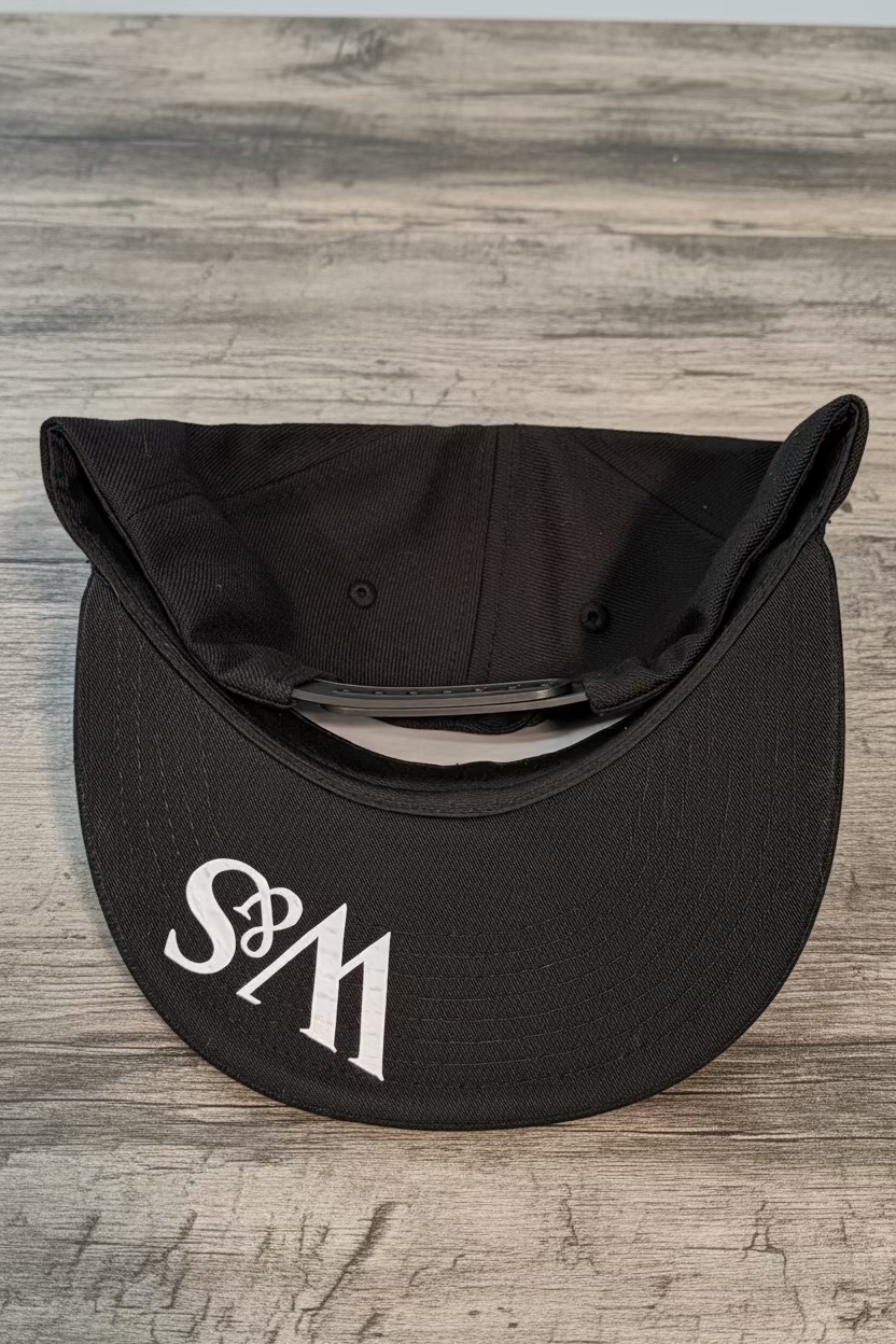 An image of the bottom of a 6 panel black snapback with the logo W&S