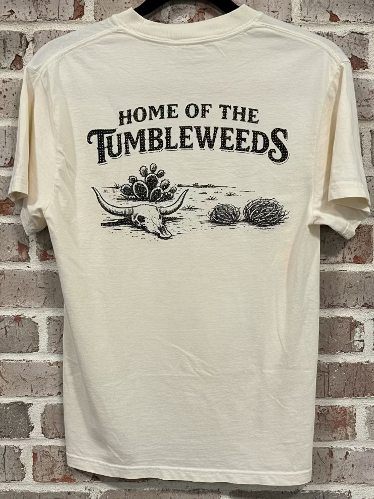 An ivory t-shirt with the words "Home of the Tumbleweeds" with a longhorn skull, cactus, and tumbleweeds against a grey backgorund