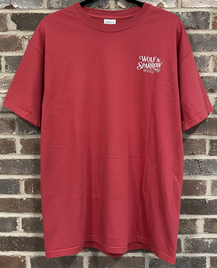 The front of a red t-shirt that has the logo Wolf & Sparrow Studio against a grey background