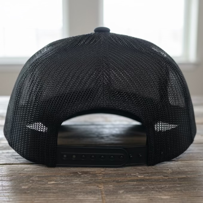 The back mesh of a black camo trucker snapback on a rustic style table with grey neutral colors